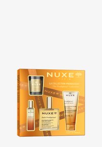 El conjunto de la colección Prodigieux de NUXE en una caja dorada incluye una vela, aceite multiusos y aceite de ducha; envases transparentes y una marca elegante.