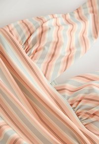 Tissu doux à rayures verticales dans des tons pastel rose, blanc, beige et marron, présentant des sections froncées et pliées.