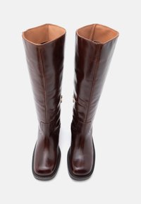 Barna bőrből készült, térd fölé érő csizmák sima felülettel, lekerekített orral, lapos talppal, és kontrasztos bézs színű bélés belül.