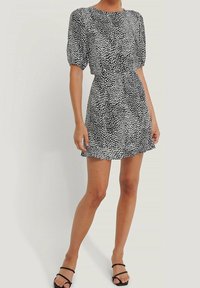 Vestido corto en blanco y negro con estampado de lunares, mangas abullonadas, escote redondo y dobladillo con volantes, hecho de tela ligera.