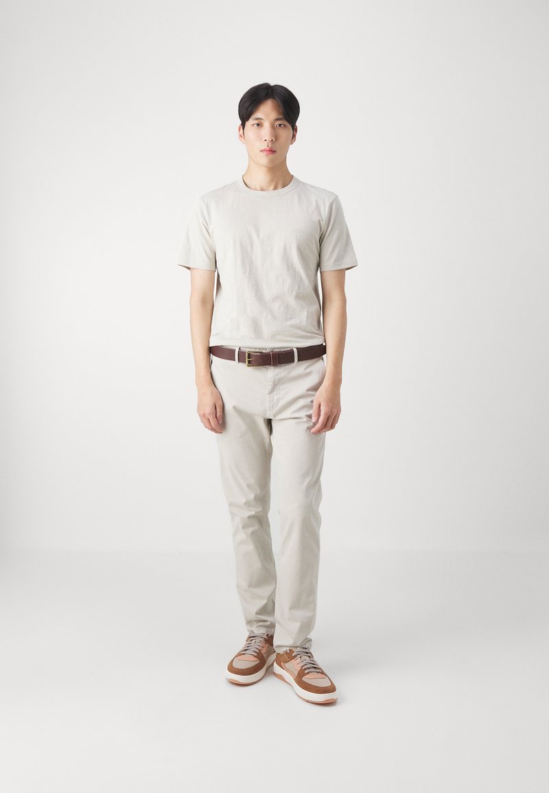 Ljust beige bomullströja ett med ljust beige byxor. Brun läderbälte och bruna sneakers med accentfärger. Enkelt design, inga mönster.