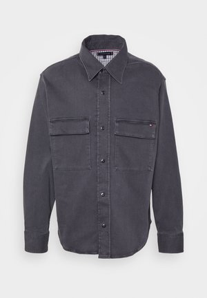 Mørkegrå skjorte med lange ærmer, knapper foran, to forlommer med klap og en spids krave.