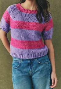 Mujer vistiendo un suéter de punto de manga corta con rayas horizontales en rosa y púrpura, combinado con unos vaqueros de cintura alta en azul.