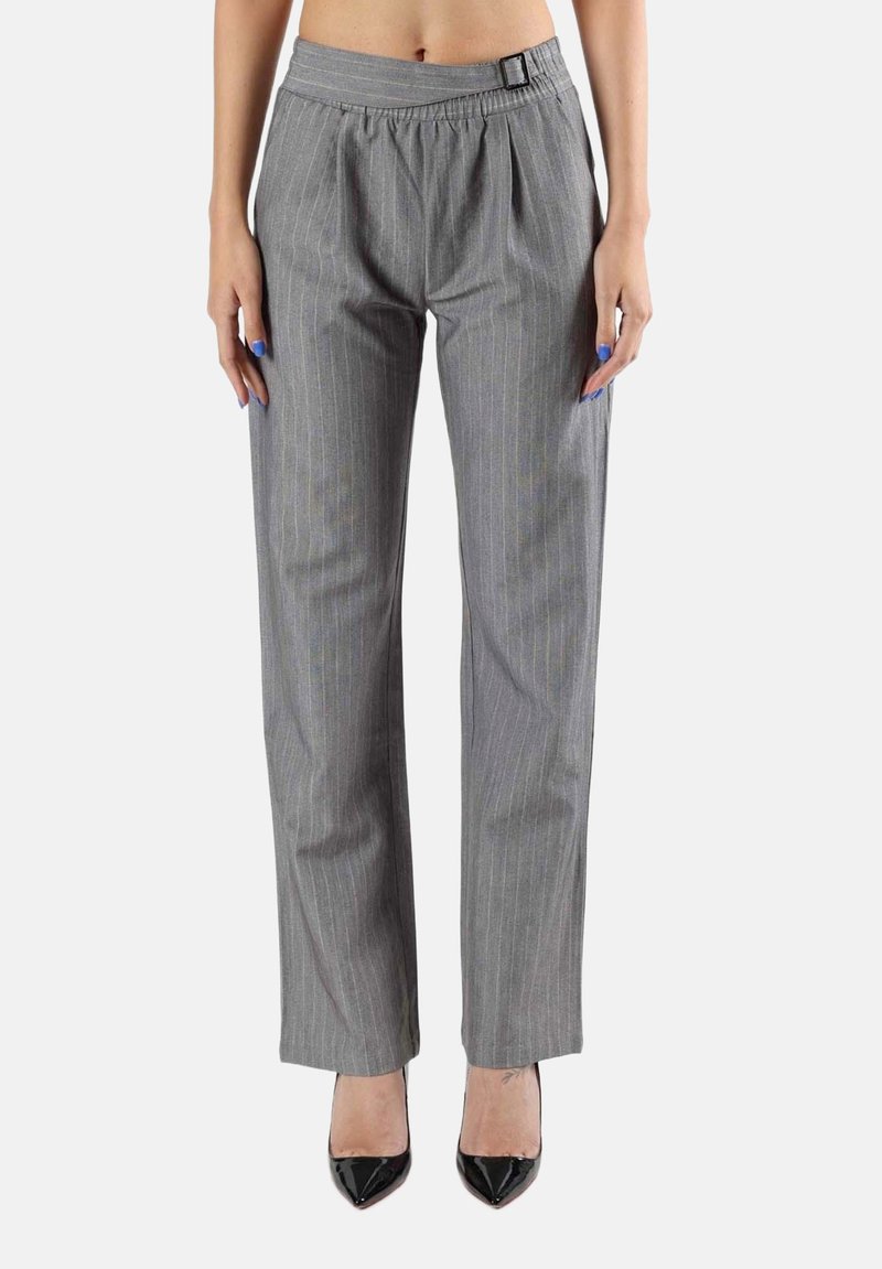 Femme portant un pantalon gris à fines rayures taille haute et jambes droites avec une boucle latérale, associé à des talons noirs à bout pointu, debout sur fond blanc.