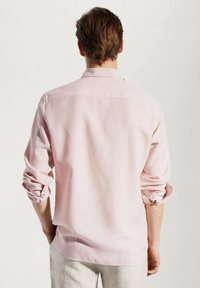 Camisa de manga larga de color rosa claro hecha de tela suave; corte relajado con puños con botones y cuello clásico; diseño minimalista, sin patrones ni detalles.
