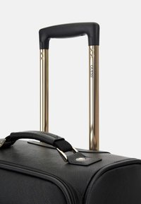 Schwarzer Koffer mit texturiertem Äußeren, goldener ausziehbarer Griff und gepolstertem Tragegurt. Strapazierfähiges Material und minimalistische Hardware-Akzente.