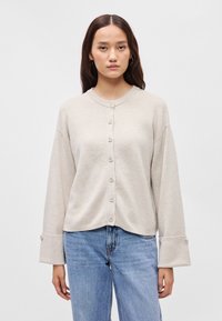 Μπεζ πλεκτό μπουφάν με στρογγυλή λαιμόκοψη, μπροστινό κούμπωμα και φαρδιές μανσέτες. Σημαντικά χαρακτηριστικά περιλαμβάνουν ριμπ πλαισίωση και μεγάλους κουμπιά.