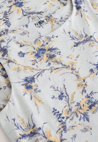 Vestido con estampado floral de tela gris claro con flores azules y amarillas, escote redondo y textura suave. Etiqueta de la marca visible: NEXT.