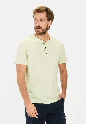 Lys grøn kortærmet henley shirt med rund halsudskæring og tre sorte knapper ved stolpen, båret med navy cargo shorts.