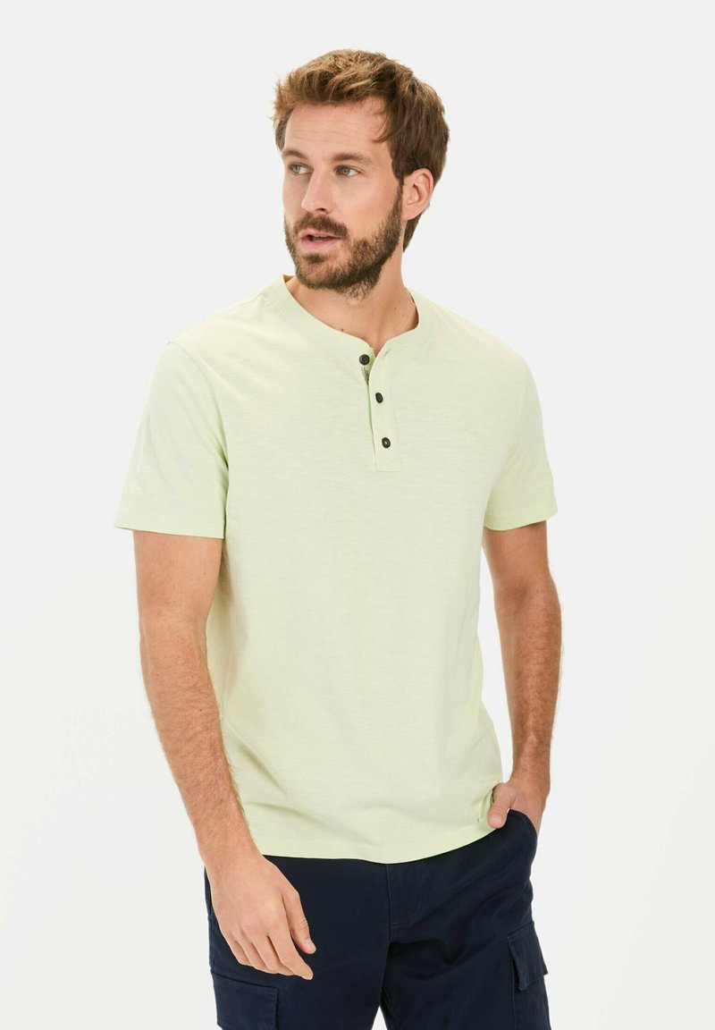 Lys grøn kortærmet henley shirt med rund halsudskæring og tre sorte knapper ved stolpen, båret med navy cargo shorts.
