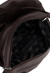 Interieur van een bruine leren tas met een gestructureerd oppervlak, voorzien van een ritsvak en een zwarte voering bedrukt met het "VENIZIA" logo.