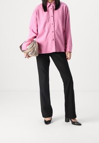 Pink oversized button-up shirt made of soft fabric, paired with tailored black pants and black patent leather heels. Silver metallic handbag.