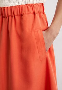 Orange skirt with a gathered elastic waistband and side pocket. Fabric appears smooth with a light texture.