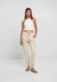 Biely skrátený halterneck top v kombinácii s béžovými nohavicami cargo, ktoré majú bočné vrecká a elastické manžety. Minimalistické sandále dotvárajú celkový vzhľad.