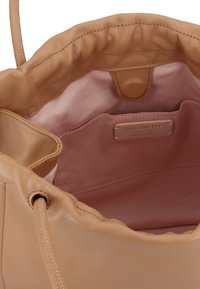 Lichtbeige leren handtas met een samengetrokken opening, een gladde textuur en een zachte voering; heeft een merkembleem en binnenzakken.