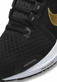 Černá sportovní obuv s prodyšným textilním svrškem, strukturovanými detaily, zlatými akcenty a bílou středovou podrážkou s nápisem "Air Zoom".