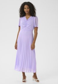 Rochie violet plisată cu mâneci pufoase scurte și un corp plisat, având o fustă fluidă și o textură transparentă. Purta sandale albe cu toc.