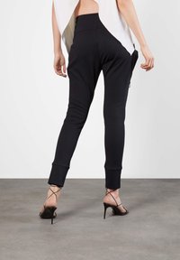 Svarta joggingsbyxor med en tapered passform, med en sidoficka med dragkedja och ribbade muddar, kombinerat med svarta högklackade sandaler med remmar.