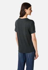 Camiseta corta de manga corta en gris oscuro con escote redondeado y un detalle de costura en la parte posterior, combinada con pantalones de mezclilla holgados.