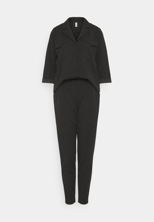 Černý overal s dlouhým rukávem, límečkem, kapsami na hrudi a zúženými nohavicemi, vystavený na jednoduchém bílém pozadí.