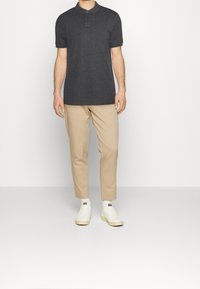 Polo shirt gris foncé avec patte de boutonnage à trois boutons, associé à un pantalon beige ajusté et des baskets blanches. Matériau lisse et design décontracté.