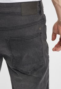 Mustad denim teksad, millel on tekstuuriga viimistlus, tagaküljel on tasku, millel on tikitud äär, ning selle kohal on ristkülikukujuline nahkmark.