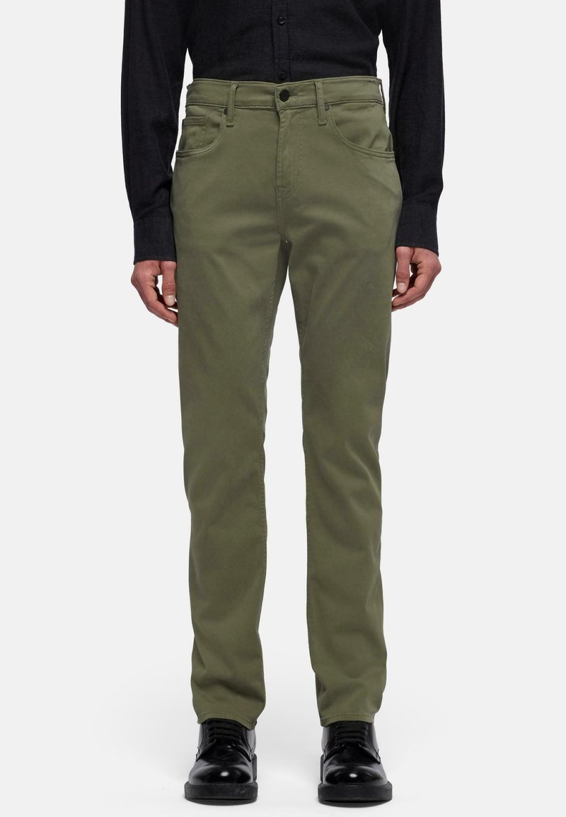 Pantaloni chino in cotone verde oliva con vestibilità slim, dotati di tasche frontali e chiusura lampo. Abbinati a scarpe eleganti nere e a una camicia nera con bottoni.