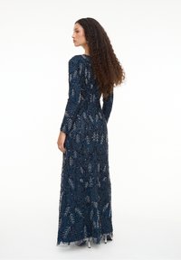 Navyblaues langes Kleid aus verziertem Stoff mit Blattmustern, langen Ärmeln und einem taillierten Oberteil, das mit silbernen Akzenten und einem schwingenden Rock versehen ist.