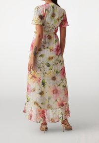 Mujer vestida con un vestido largo, floral, de manga corta y con un dobladillo con volantes, mostrado desde atrás.