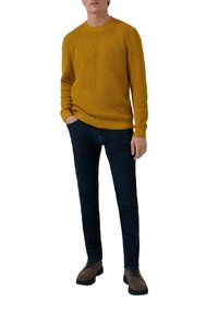 Żółty sweter o fakturowej strukturze, okrągły dekolt, ściągacze na rękawach i u dołu, w połączeniu z ciemnoniebieskimi dżinsami i brązowym obuwiem. Ubranie w stylu casual.