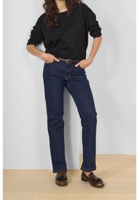 Pull noir surdimensionné, jean droit bleu marine, mocassins marron. Textures de tissu lisses, coupe décontractée, design classique.