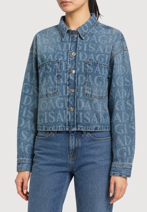 Frau trägt eine cropped blaue Denimjacke mit Knopfverschluss und großen Fronttaschen, kombiniert mit passenden blauen Denim-Jeans.