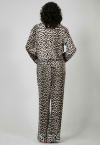 Pyzamový set s leopardím vzorom vyrobený z mäkkej látky, s dlhými rukávmi, voľnými nohavicami a čiernym lemovaním okolo manžiet, ktorý vystihuje voľný dizajn.