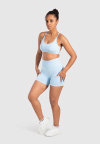 Lichtblauwe sportbeha met verstelbare banden, gecombineerd met high-waisted shorts. De stof is glad met een getailleerd ontwerp, verfraaid met subtiele stiksels.
