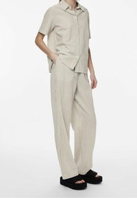 Short-sleeve, collared shirt and wide-leg pants in beige with vertical stripes. Textured fabric. Worn with black platform sandals.