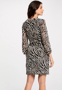 Abito con stampa zebra nera e crema, maniche lunghe e trasparenti, vita aderente e lunghezza fino a metà coscia, realizzato in un materiale leggero.