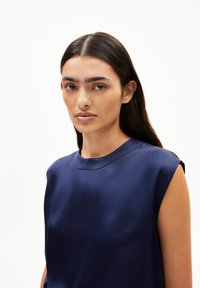 Navy blue satin sleeveless top with a round neck and subtle sheen, featuring a relaxed fit and minimal details. Smooth texture.