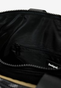 Schwarze Stofftasche mit einem Reißverschlussfach im Inneren, glatte Textur und einem Markenschild. Verfügt über einen Reißverschlussverschluss und organisierte Fächer.