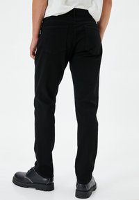Jeans de mezclilla negra con un ajuste slim, que presentan una cintura de altura media, dos bolsillos traseros y detalles de costura sutiles. Combinados con botas negras con cordones.