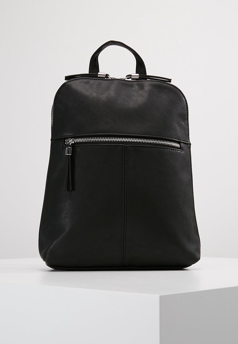 Sac à dos en cuir noir avec poignée supérieure, poche avant zippée et fermeture éclair argentée sur un fond clair uni sur une surface blanche.