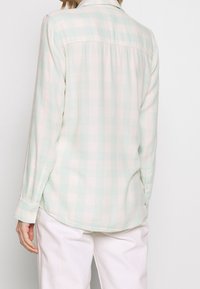 Camisa de cuadros de color verde menta y rosa claro, de manga larga y con botones, que presenta una tela suave, un dobladillo curvado y puños abotonados.