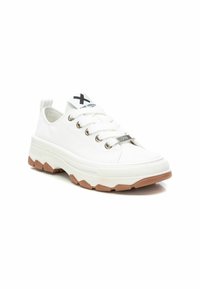 Zapatillas de lona blancas con puntera redonda, ojales de metal, cordones blancos y una suela de goma gruesa y texturizada. Logo negro en la lengüeta.