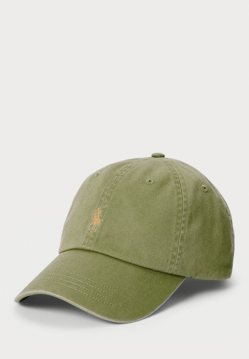 Green cotton baseball cap with a curved visor. Features embroidered logo in light yellow, ventilation holes, and an adjustable strap at the back.
