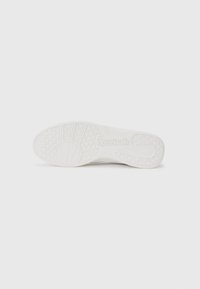 Talpa de pantof sport albă, dotată cu un cauciuc texturat pentru aderență, având un branding proeminent "Reebok" și un model de profil circular.