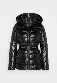 Chaqueta de plumón negra brillante con capucha, cremallera frontal, bolsillos laterales y cinturón negro con el logo de "Calvin Klein" en la hebilla y el pecho.