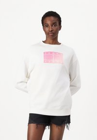 Witte fleece sweatshirt met een roze rechthoekig grafisch ontwerp met de tekst "TOMMY JEANS". Zachte stof, relaxte snit en geribbelde halslijn.