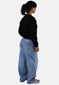 Wide-leg light blue jeans made from denim, paired with a black long-sleeve shirt. Features back pockets and a casual fit.