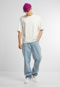 Fehér túlméretezett póló, világoskék bő szabású farmernadrág, fehér sportcipő és lila kötött sapka. Minimalista design, lágy textúrákkal.