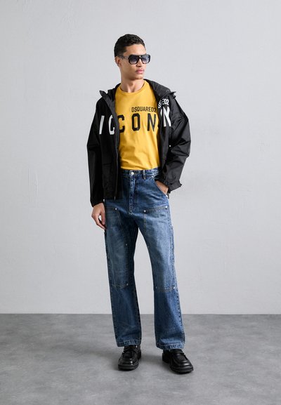 Veste noire avec le texte blanc "ICON", t-shirt jaune, jean en denim bleu, chaussures noires et lunettes de soleil. Tenue décontractée avec des textures variées.
