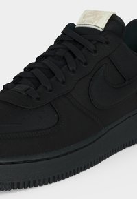 Μαύρο χαμηλό παπούτσι Nike με μαύρα κορδόνια, ανάγλυφο λογότυπο Nike swoosh στο πλάι και αντίθετο λευκό ετικέτα με το λογότυπο Nike στη γλώσσα.
